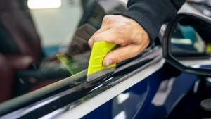 Audi S5 chrome delete. Progress photo of wrapping the front door window trim. Using a squeegee to tuck the film behind the window rubber. Photo two.