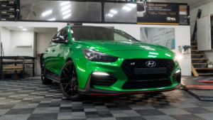 Hyundai i30N wrapped in 3M Gloss Green Envy with Gloss Black roof and side stripes. Exterior photo of the front.