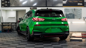 Hyundai i30N wrapped in 3M Gloss Green Envy with Gloss Black roof and side stripes. Exterior photo of rear.