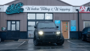 Land Rover Defender OCTA - 3M Satin Black. Photo of the front of the car from outside the shop.